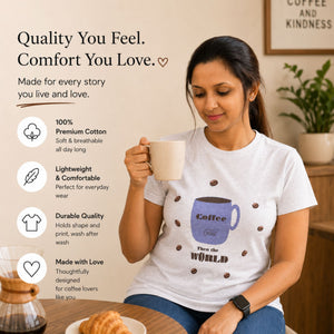 Woman holding a coffee mug wearing a t-shirt with a coffee cup design, sitting at a table with a plant in the background.