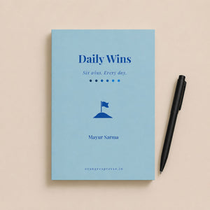 Blue book titled 'Daily Wins' with a pen on a beige background