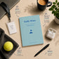 Notebook titled 'Daily Wins' on a desk with a cup of coffee, laptop, and other items.