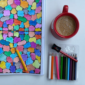 Colorful coloring book with a red mug of coffee and colored pencils on a white surface