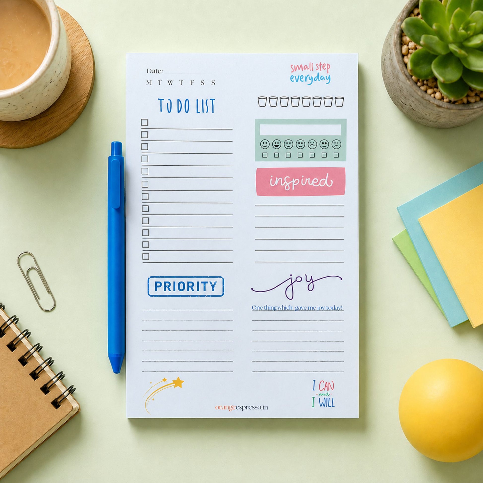 A daily to-do list planner page from OrangePress is shown in a styled flat-lay setting with a blue pen, a coffee cup, a succulent, sticky notes, and a notebook on a pale green background.